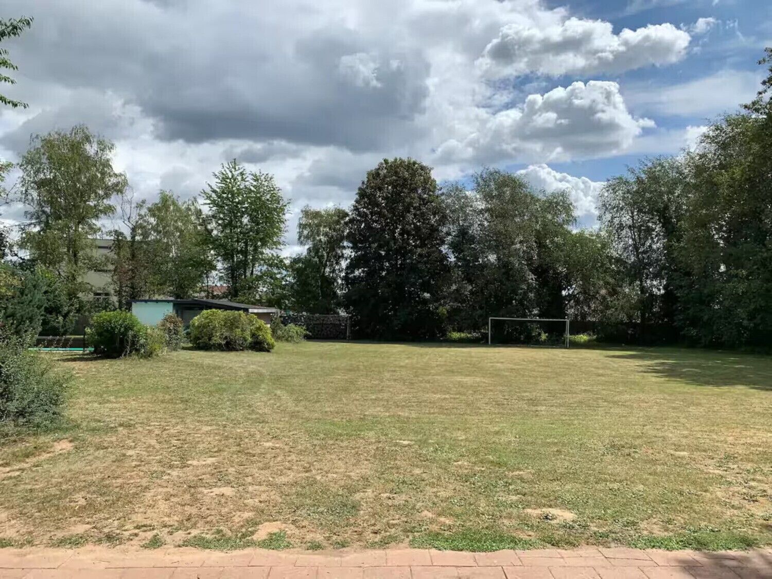 Un espace extérieur verdoyant avec des poteaux de but, des arbres et un bâtiment en arrière-plan.