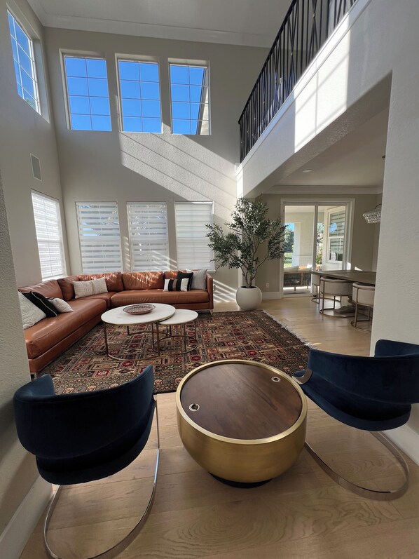 A spacious living area with a brown leather sofa, a round wooden coffee table, and two blue chairs. - Luxurious Golf Course Retreat - Fully Remodeled near Napa and San Francisco (Fairfield)
