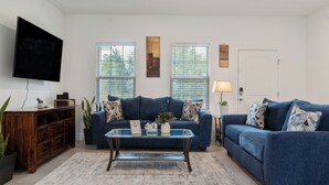 Ein Wohnzimmer mit einem blauen Sofa, einem Glastisch und einem an der Wand montierten Flachbildfernseher.
