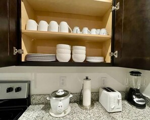 Eine Küche mit Arbeitsplatte, Kaffeemaschine, Toaster, Mixer und einem Regal mit weißen Geschirr.
