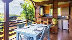 A wooden deck with a table set for dining, a small kitchen area, and a view of lush greenery. - Wooden bungalow Ti Briz - Au jardin d'Éole (Sainte-Rose)