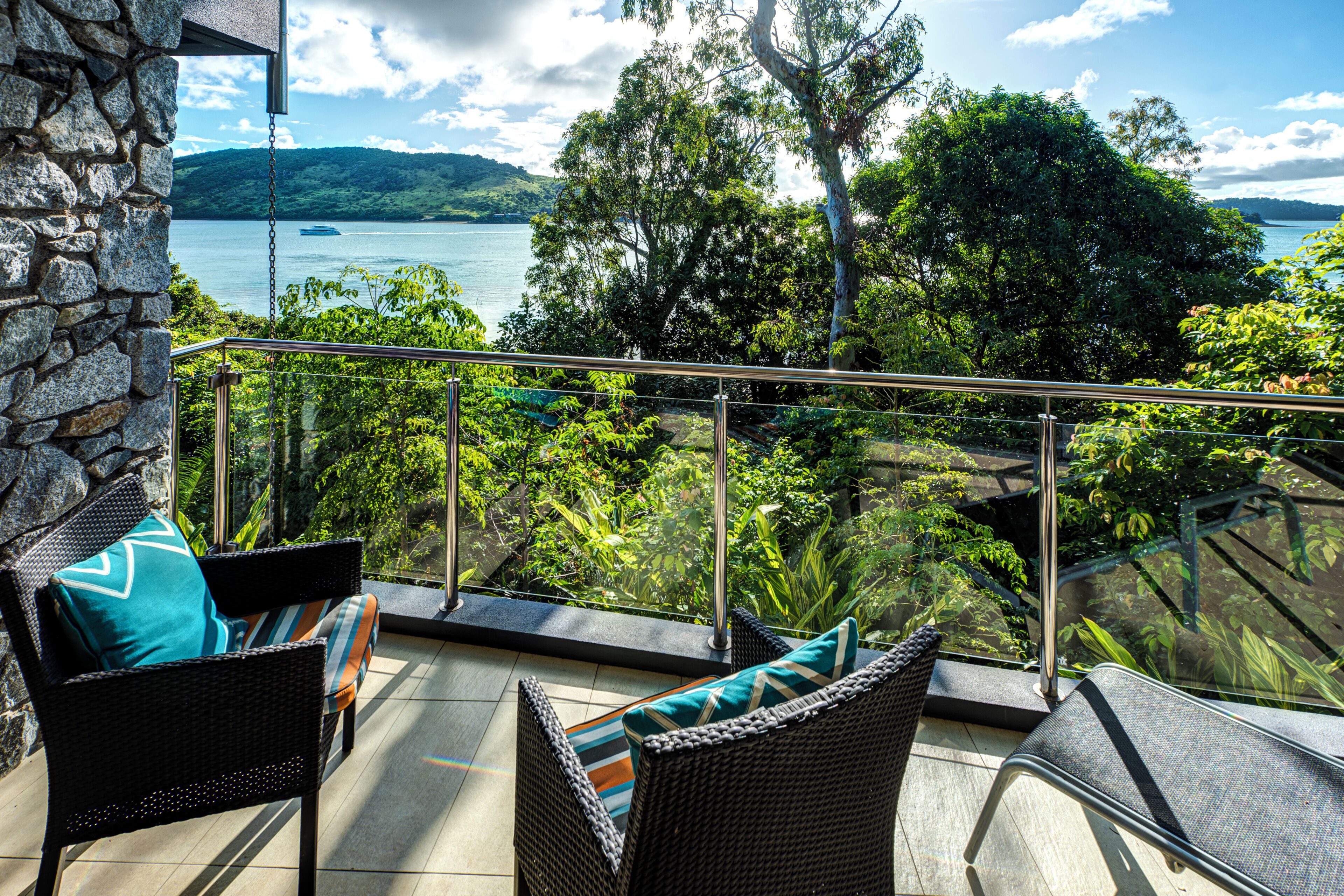 Ein Balkon mit Korbmöbeln und einer Steinmauer mit Blick auf einen See und üppiges Grün.