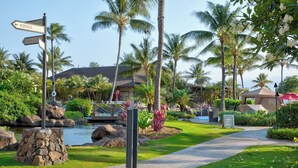 A tropical resort with a stone path, palm trees, and a signpost indicating directions to Kona and Aina Coi.