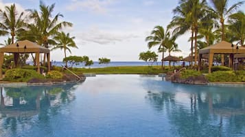 A pool area with two gazebos, palm trees, and a view of the ocean.