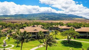 A resort with multiple buildings, palm trees, and a mountainous backdrop.
