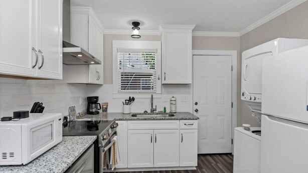 Una cocina compacta con armarios blancos, microondas, cafetera y refrigerador.
