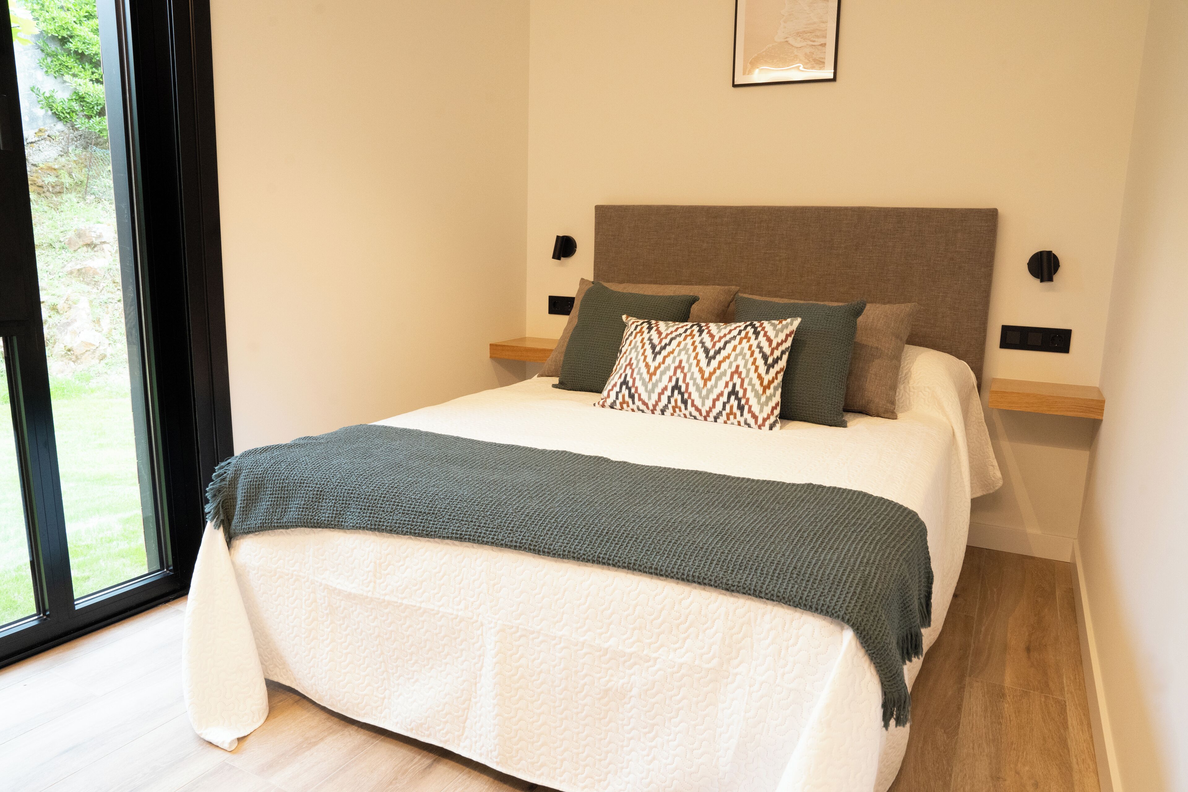 Une chambre à coucher avec un lit, des oreillers, une tête de lit, des tables de chevet et une fenêtre.