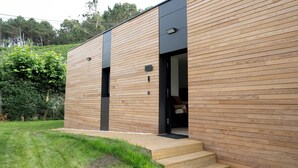 A modern building with wooden paneling and black accents. There are steps leading to a door and a small outdoor area with a bench. - Balcobo Villas&Cabañas (Arteixo)