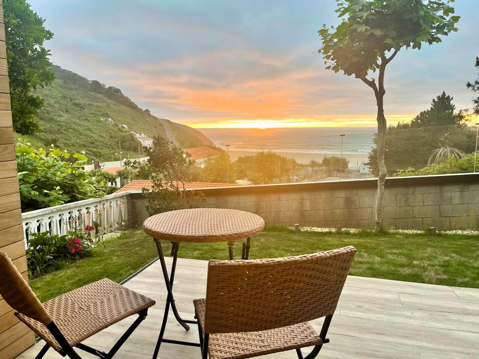 A patio with wicker furniture and a view of the ocean at sunset.