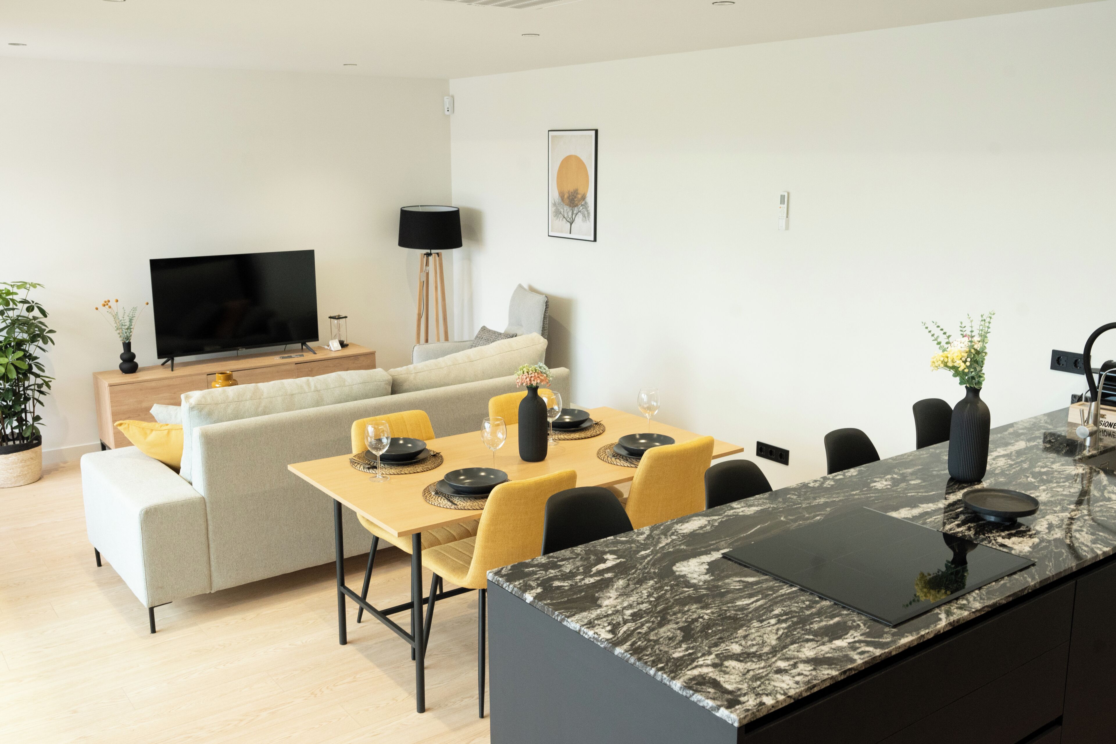A modern living room with a sofa, a TV, a dining table set for four, and a kitchen island.