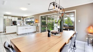 A modern kitchen with a central island, a dining area with a wooden table, and a large window providing a view of greenery.