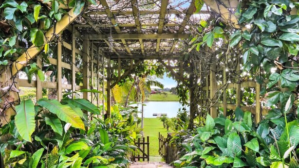 A garden pathway leading to a gazebo with a view of a lake.