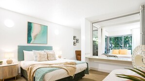 A modern bedroom with a large bed, a view of the outdoors through a window, and a small seating area with a view.