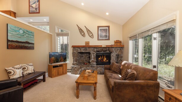 A cozy living room with a stone fireplace, a comfortable sofa, a wooden coffee table, and a television on a wooden stand. - Private Home with Hot Tub in Keystone (Dillon)