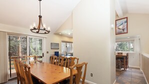 A dining area with a large wooden table and chairs, a chandelier, and a view of the outdoors through large windows. - Private Home with Hot Tub in Keystone (Dillon)
