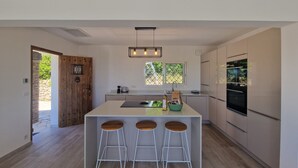 Une cuisine moderne dotée d’un îlot central, de tabourets de bar, d’un four encastré et d’une fenêtre donnant sur un espace verdoyant.