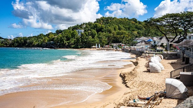 Una playa con agua turquesa cristalina, orilla arenosa y colinas verdes exuberantes al fondo.