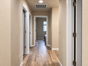 Un couloir doté d’un plancher en bois, de murs blancs et d’une grille d’aération au plafond.