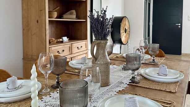 Un coin repas avec une table en bois dressée pour le repas, un buffet en bois et un miroir au mur.