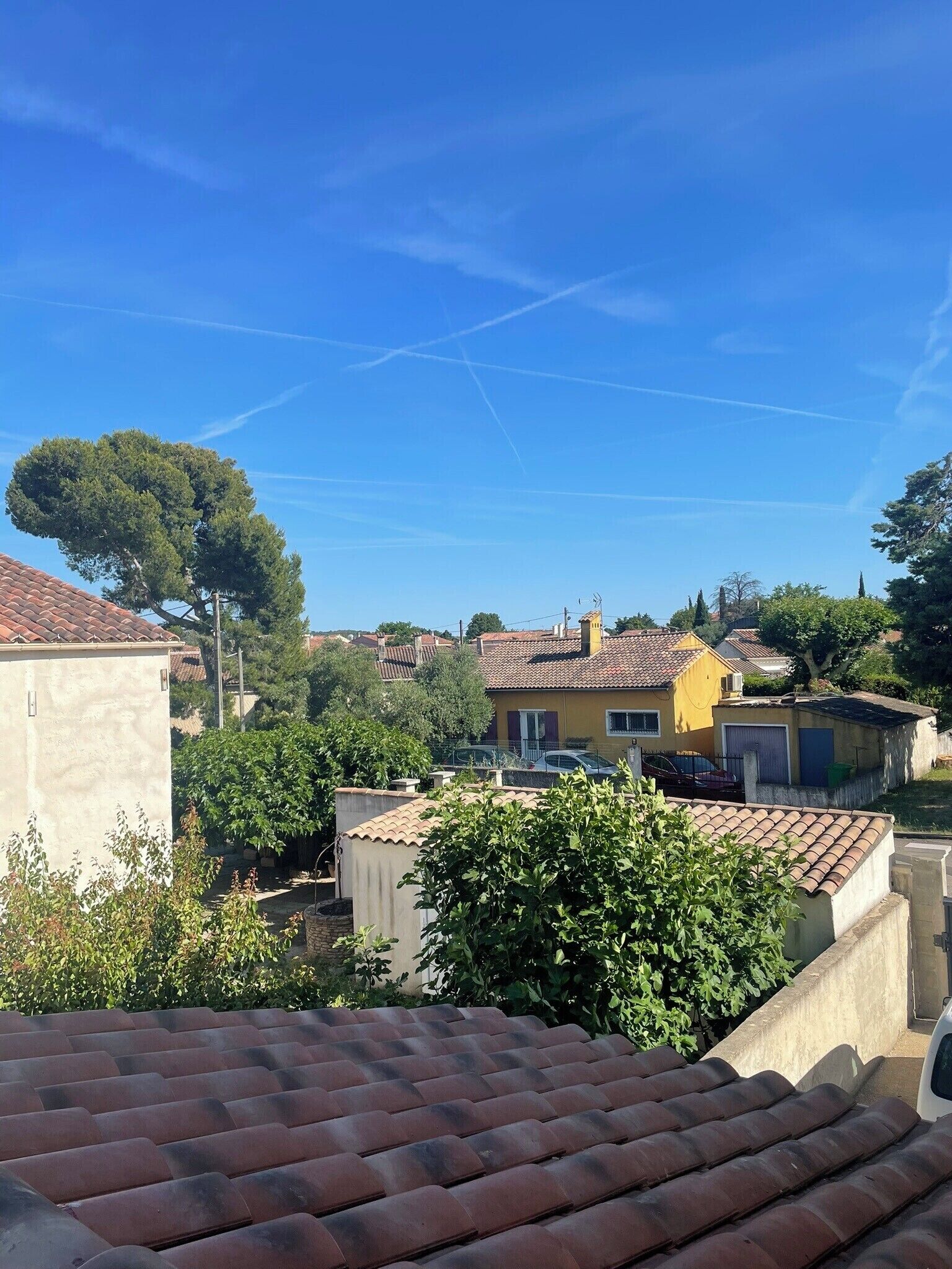 Un quartier résidentiel caractérisé par des toits recouverts de tuiles en terre cuite, une maison jaune et une végétation luxuriante.