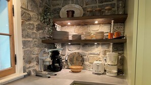 Una cocina con paredes de piedra, una cafetera, un tostador y estantes con platos y tazas.