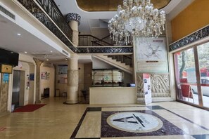 Rebedor d'hotel amb una ostentosa pèndol, una taula de recepció, una escala i un gran emblema circular al sòl.