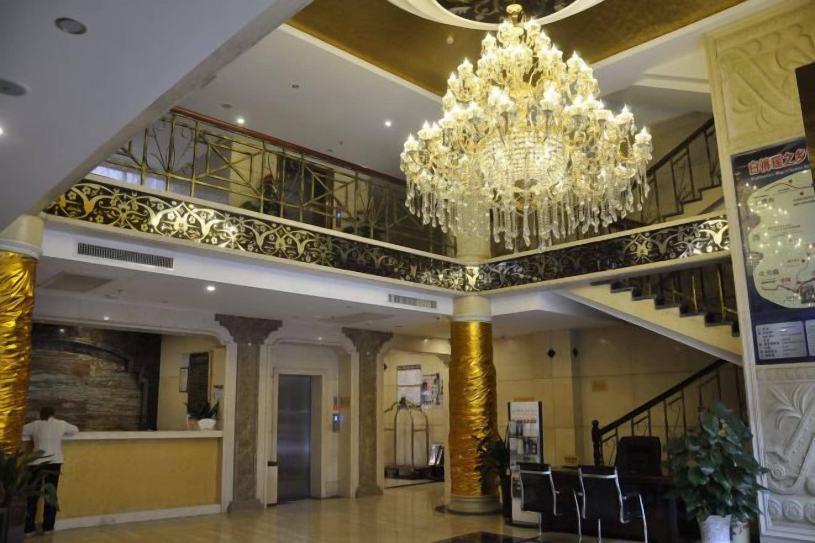 A hotel lobby with a grand chandelier, a reception desk, and a staircase.