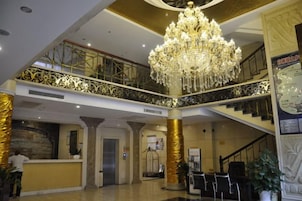 Un vestíbulo de hotel con una suntuosa araña, un mostrador de recepción y una escalera.
