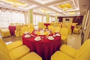 A banquet hall with round tables, yellow chairs, and red tablecloths.
