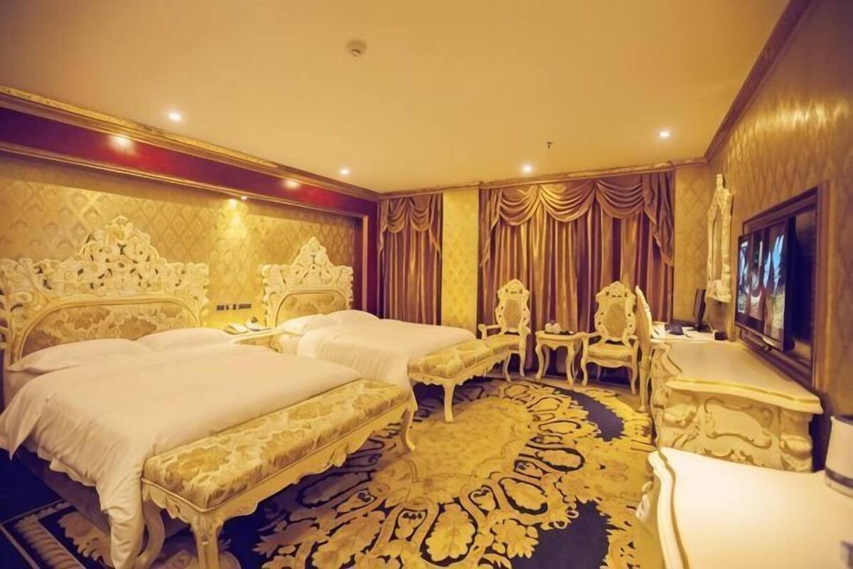 Habitación de hotel con dos camas, una zona de estar con una silla y una mesa, televisión y una alfombra estampada.