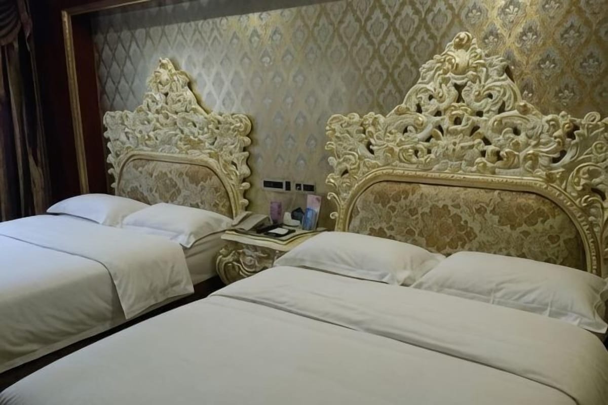 A hotel room with two beds, ornate headboards, a nightstand, and a mirror.