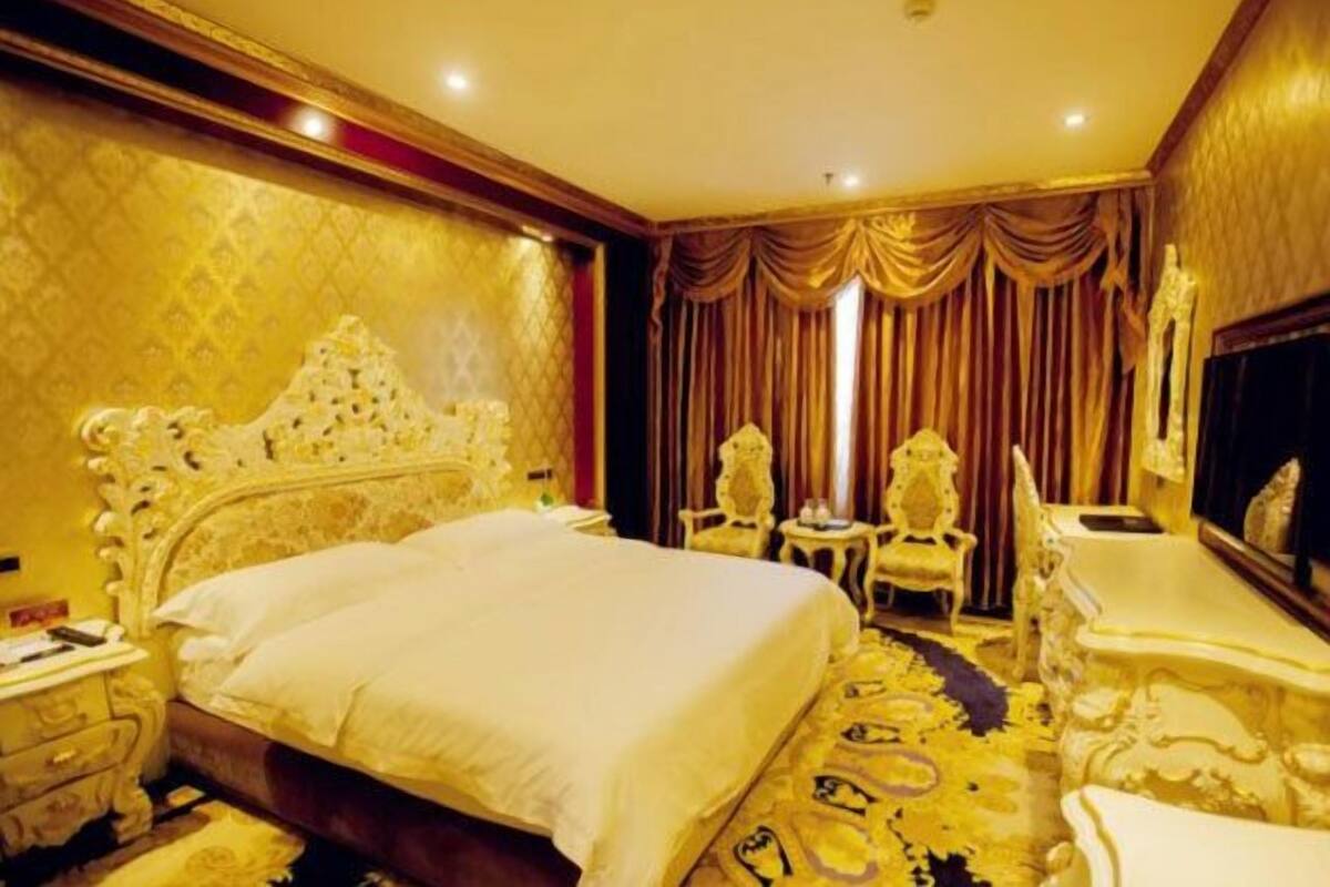 Una lujosa habitación de hotel con una cama grande y ornamentada, una zona de estar con sofá y sillones, y una televisión.