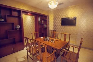 A dining area with a wooden table and chairs, a chandelier, and a TV mounted on the wall. - Alps hotel (Nandan)