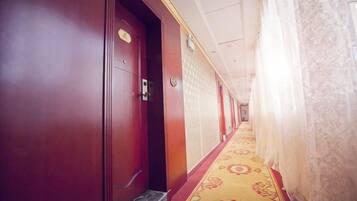 A hotel corridor with a patterned carpet, wooden doors, and a red wall.