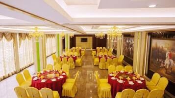 A banquet hall with round tables, yellow chairs, and red tablecloths.