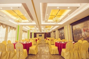 Un salón de banquetes con mesas redondas, sillas amarillas, candelabros y un cuadro grande en la pared.