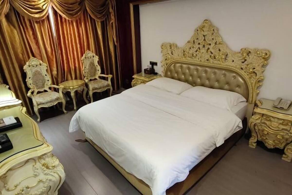 Una cama grande con cabecera acolchada, dos mesitas de noche y dos sillas decorativas.