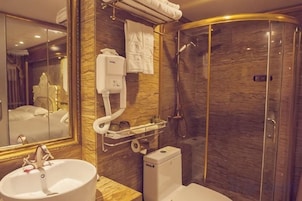 Un baño con lavamanos, espejo, dispensador de toallas y cabina de ducha.
