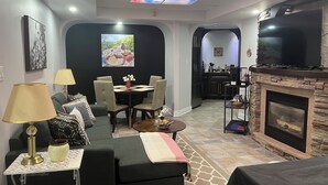 A modern living room with a fireplace, a dining area, and a kitchen visible through an archway. - Serene & Luxurious  basement apartment. (Timmins)
