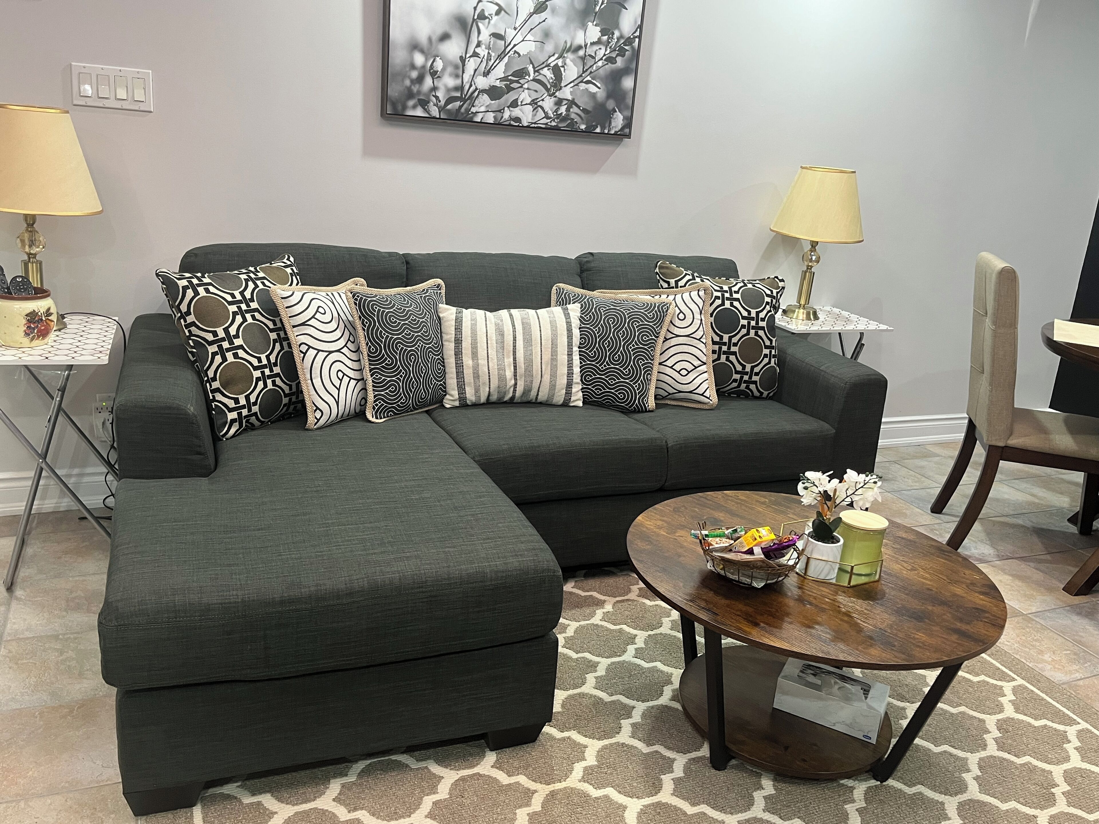 A modern living room with a sectional sofa, patterned throw pillows, a round coffee table with decorative items, and two floor lamps.