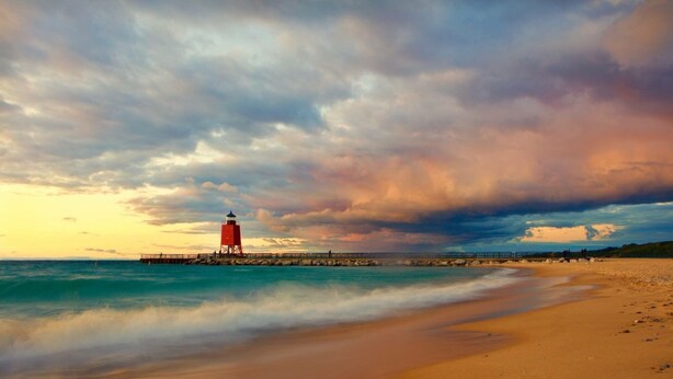 A beach with a red lighthouse and a pier extending into the water.