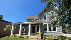 A two-story house with a covered porch, a brick wall adjacent to it, and a well-maintained lawn.