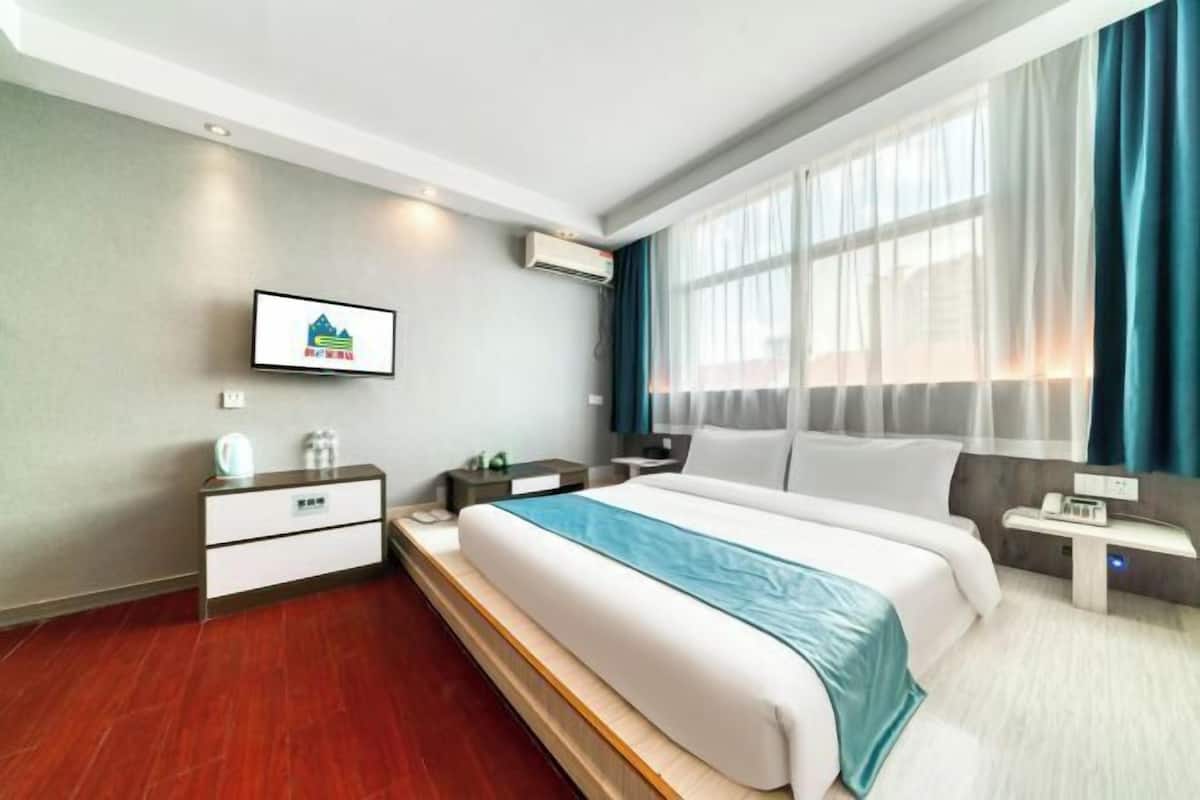 Une chambre d’hôtel moderne, dotée d’un grand lit, d’une table de chevet, d’une commode, d’un téléviseur et d’une fenêtre avec des rideaux.