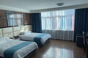 Habitación de hotel con dos camas, pared de ladrillo decorativa, un ventanal con cortinas y suelo de madera.