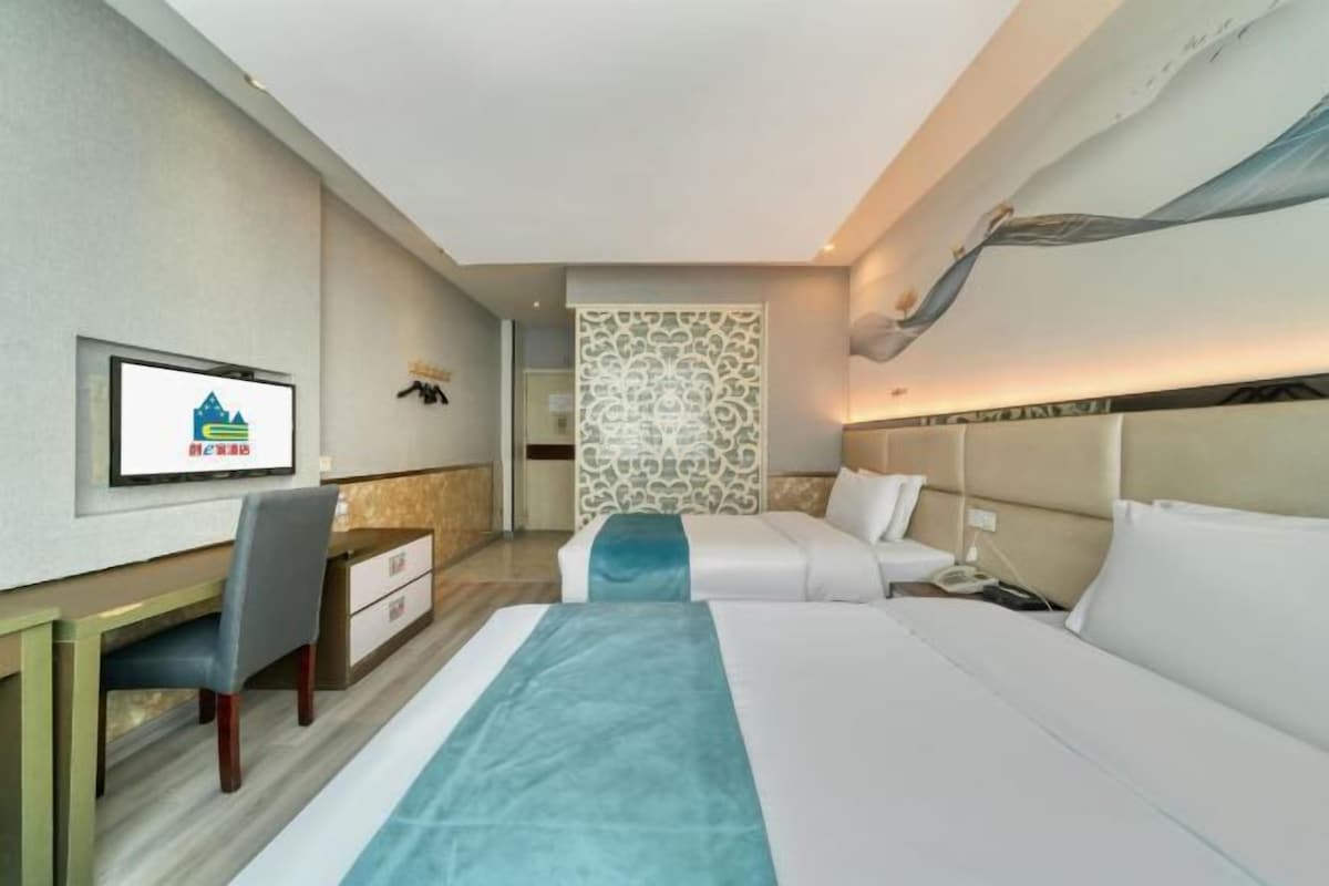 Habitación de hotel con cama, escritorio, silla, televisor y un panel decorativo en la pared.