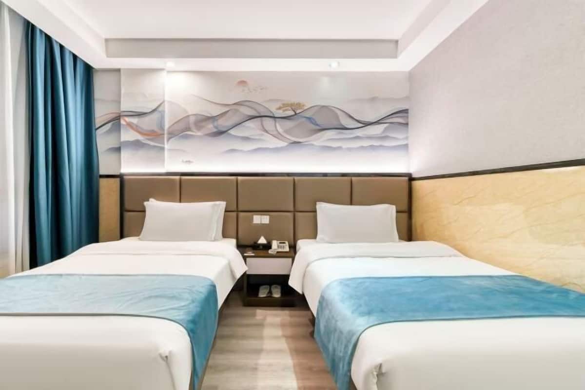 Une chambre d’hôtel avec deux lits, une tête de lit ornée d’un panneau décoratif, une table de chevet et une paire de pantoufles.