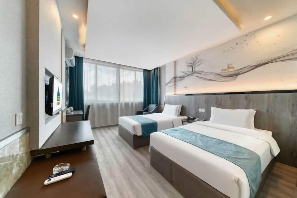 Une chambre d’hôtel avec deux lits, un bureau, une télévision et une grande fenêtre avec des rideaux.