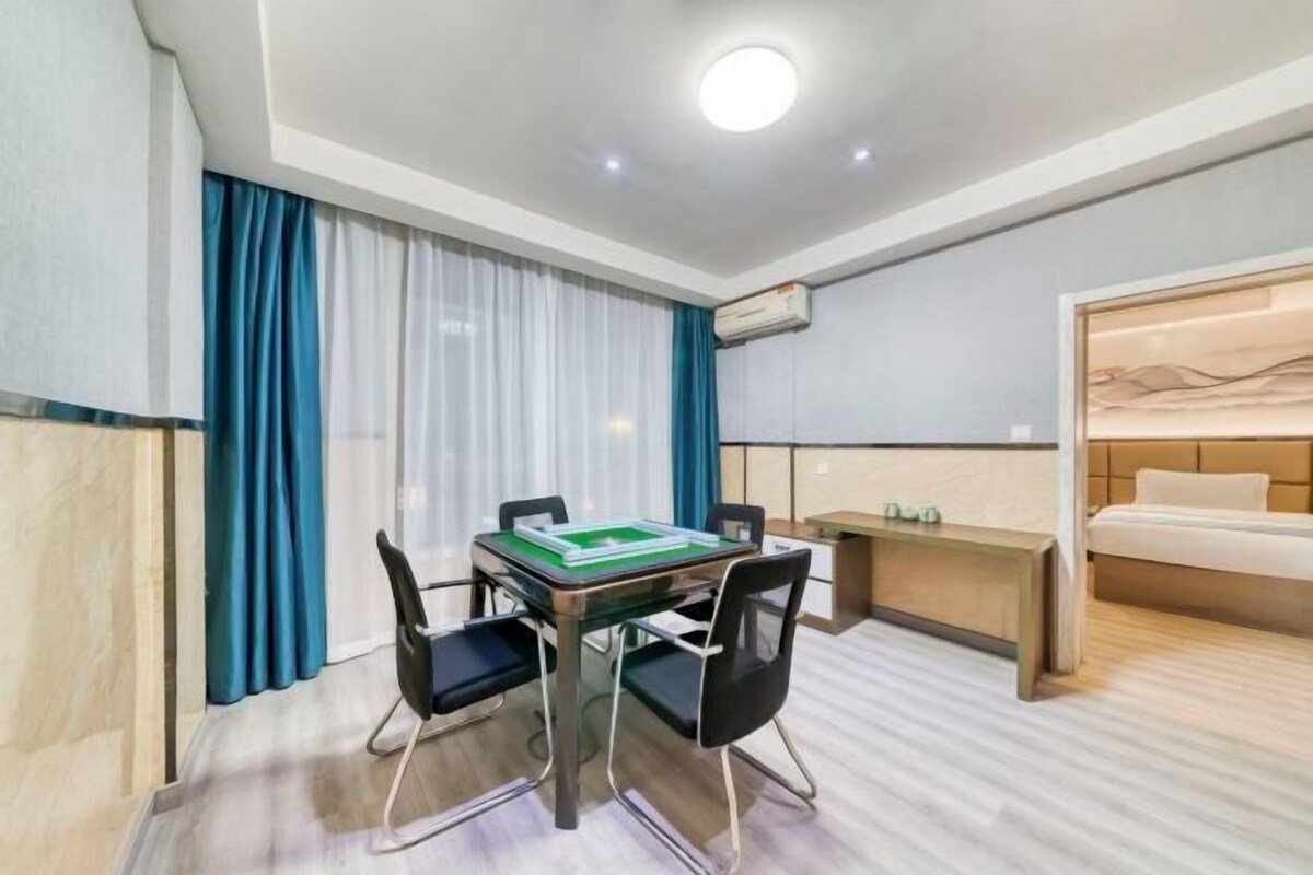 Una habitación de hotel con una mesa de comedor, sillas, una cama, una mesita de noche y un ventanal con cortinas.