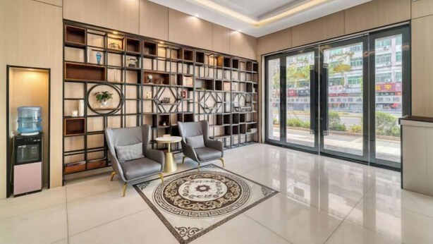 A modern hotel lobby with a large bookshelf, two armchairs, a small round table, and a large window offering a view of the outside. - Chuangejia Yuerongzhuang Hotel (Yongkang East Bus Station Exhibition Center) (Yongkang)