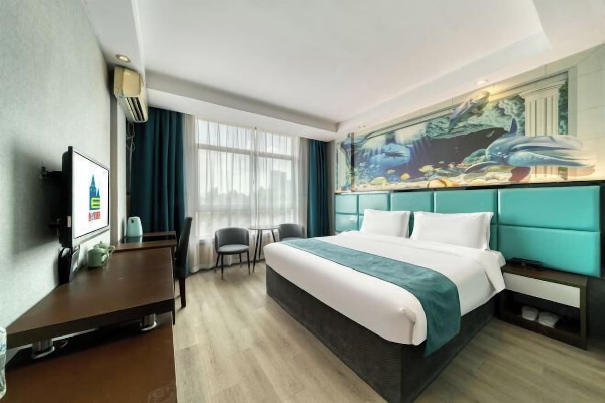 Una habitación de hotel moderna con una cama grande, un escritorio, un televisor y un mural con vida marina en la pared.